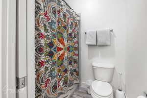 Bathroom featuring toilet, curtained shower, baseboards, and wood finished floors