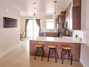 Kitchen with a breakfast bar area, a peninsula, hanging light fixtures, stainless steel appliances, and light countertops