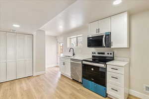 Kitchen featuring light wood finished floors, appliances with stainless steel finishes, a sink, and white cabinetry