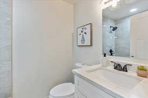 Bathroom featuring a tile shower, vanity, and toilet