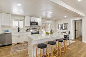 Kitchen featuring appliances with stainless steel finishes, a kitchen island, white cabinetry, and light stone countertops