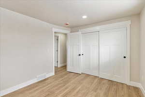 Unfurnished bedroom with light wood finished floors, baseboards, visible vents, and a closet