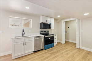 Kitchen with stainless steel appliances, a sink, white cabinetry, light countertops, and light wood finished floors