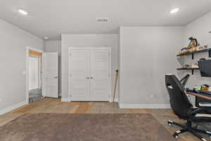 Office area with light wood-style floors, baseboards, visible vents, and recessed lighting