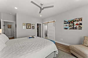 Bedroom featuring a barn door, baseboards, a ceiling fan, wood finished floors, and recessed lighting