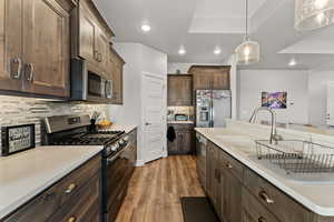 Kitchen featuring wood finished floors, decorative light fixtures, stainless steel appliances, light countertops, and a sink