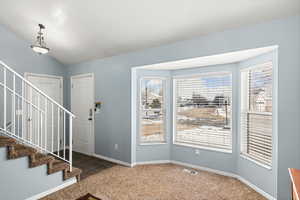 Carpeted entryway with stairway, baseboards, visible vents, and vaulted ceiling