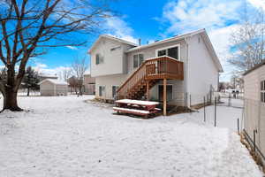 Snow covered house featuring stairway, fence, and a wooden deck