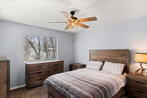 Bedroom featuring a ceiling fan, dark carpet, a textured ceiling, and baseboards