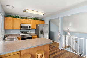 Kitchen featuring light countertops, appliances with stainless steel finishes, dark wood-type flooring, a sink, and a kitchen bar