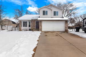 View of front of house featuring driveway, brick siding, and fence