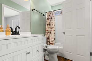 Bathroom featuring toilet, shower / tub combo, wood finished floors, and vanity