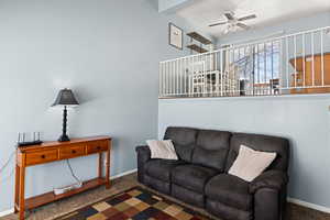 Carpeted living room featuring ceiling fan, beamed ceiling, and baseboards