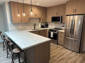 Newly updated kitchen featuring decorative light fixtures, a breakfast bar area, appliances with stainless steel finishes, a sink, and a peninsula