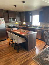 Kitchen with dark brown cabinetry, light wood-style flooring, appliances with stainless steel finishes, decorative light fixtures, and a center island