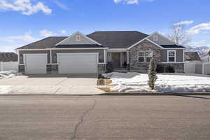 Craftsman-style home featuring a shingled roof, an attached garage, fence, stone siding, and driveway