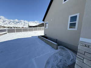 View of snowy exterior featuring fence, a mountain view, and stucco siding