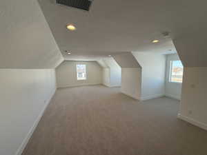 Bonus room featuring visible vents, light carpet, vaulted ceiling, a textured ceiling, and baseboards