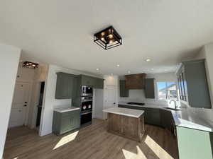 Kitchen featuring stainless steel microwave, a center island, black gas cooktop, light countertops, and a sink