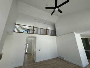 Unfurnished room featuring baseboards, visible vents, ceiling fan, a high ceiling, and light wood-style floors