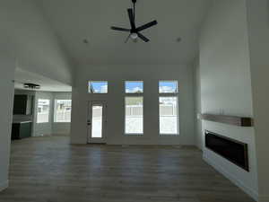 Unfurnished living room with baseboards, high vaulted ceiling, dark wood-type flooring, and a glass covered fireplace