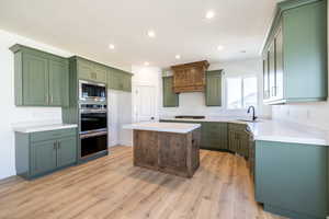 Kitchen with stainless steel appliances, light wood-type flooring, recessed lighting, a kitchen island, and light countertops