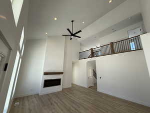 Unfurnished living room featuring baseboards, a glass covered fireplace, ceiling fan, light wood-style flooring, and high vaulted ceiling