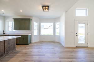 Kitchen featuring green cabinetry, light countertops, light wood-style flooring, recessed lighting, and a textured ceiling