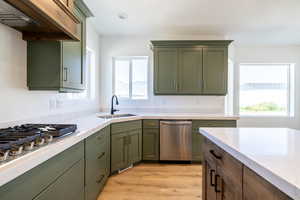 Kitchen featuring appliances with stainless steel finishes, green cabinets, under cabinet range hood, light countertops, and healthy amount of natural light