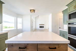 Kitchen with green cabinetry, double oven, built in microwave, light wood-type flooring, and a kitchen island