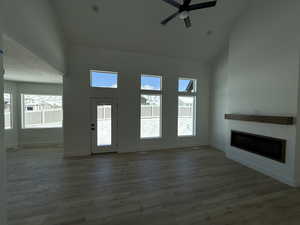 Unfurnished living room with baseboards, a ceiling fan, a glass covered fireplace, wood finished floors, and high vaulted ceiling