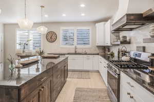 Kitchen with stainless steel range with gas cooktop, custom exhaust hood, pendant lighting, and dark stone countertops