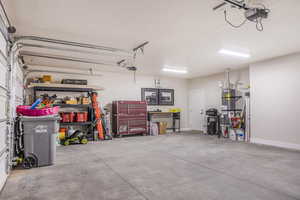 Garage featuring a garage door opener, strapped water heater, and baseboards