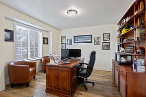 Office with a textured ceiling, light wood-type flooring, and baseboards