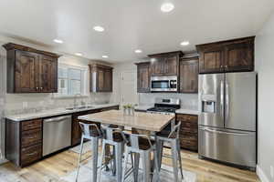 Kitchen with a breakfast bar area, light wood finished floors, stainless steel appliances, a sink, and dark brown cabinets