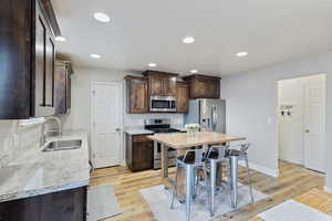 Kitchen with light wood finished floors, a breakfast bar area, stainless steel appliances, recessed lighting, and a sink