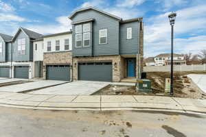 View of property with driveway, stone siding, an attached garage, and central AC unit