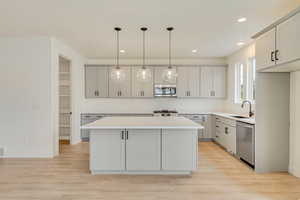 Kitchen with pendant lighting, light countertops, appliances with stainless steel finishes, a kitchen island, and a sink