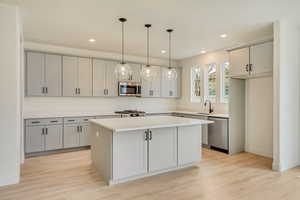 Kitchen featuring a kitchen island, light countertops, appliances with stainless steel finishes, light wood-type flooring, and decorative light fixtures