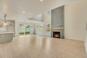 Unfurnished living room featuring light wood finished floors, visible vents, a glass covered fireplace, a chandelier, and recessed lighting