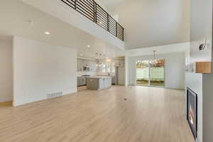 Unfurnished living room featuring visible vents, light wood-style flooring, a chandelier, a warm lit fireplace, and baseboards