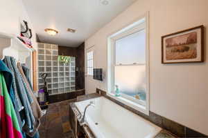 Bathroom featuring a garden tub, stone tile floors, and visible vents