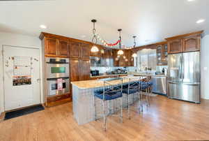 Kitchen with a kitchen island, glass insert cabinets, appliances with stainless steel finishes, light stone counters, and pendant lighting