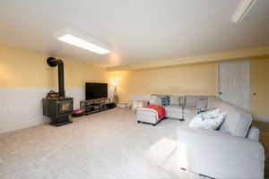 Carpeted living area featuring a wood stove and wainscoting