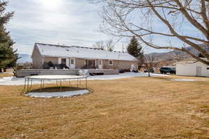 Rear view of property featuring a trampoline, a lawn, and a deck