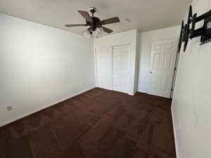 Unfurnished bedroom with ceiling fan, dark carpet, and a closet