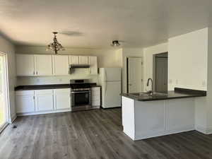 Kitchen featuring sink, gas range, white refrigerator, kitchen peninsula, and white cabinets