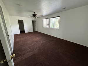 Unfurnished bedroom featuring ceiling fan, dark carpet, and a textured ceiling