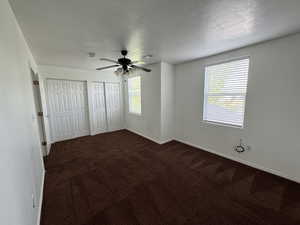 Unfurnished bedroom with ceiling fan, dark carpet, a textured ceiling, and two closets