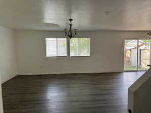 Empty room with dark wood-type flooring, a notable chandelier, and a textured ceiling